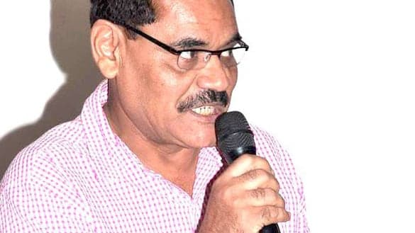 Mushtaq Khan speaking into a microphone at a Mumbai event in 2012, in a pink checked shirt and glasses.