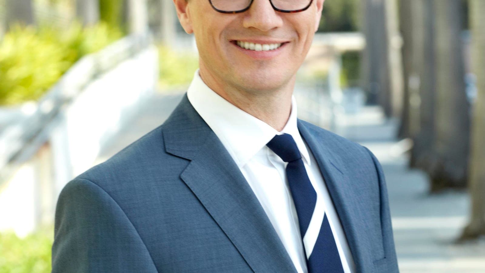 Peter Rice, in a grey suit and navy striped tie, photographed smiling on a palm-lined Los Angeles street