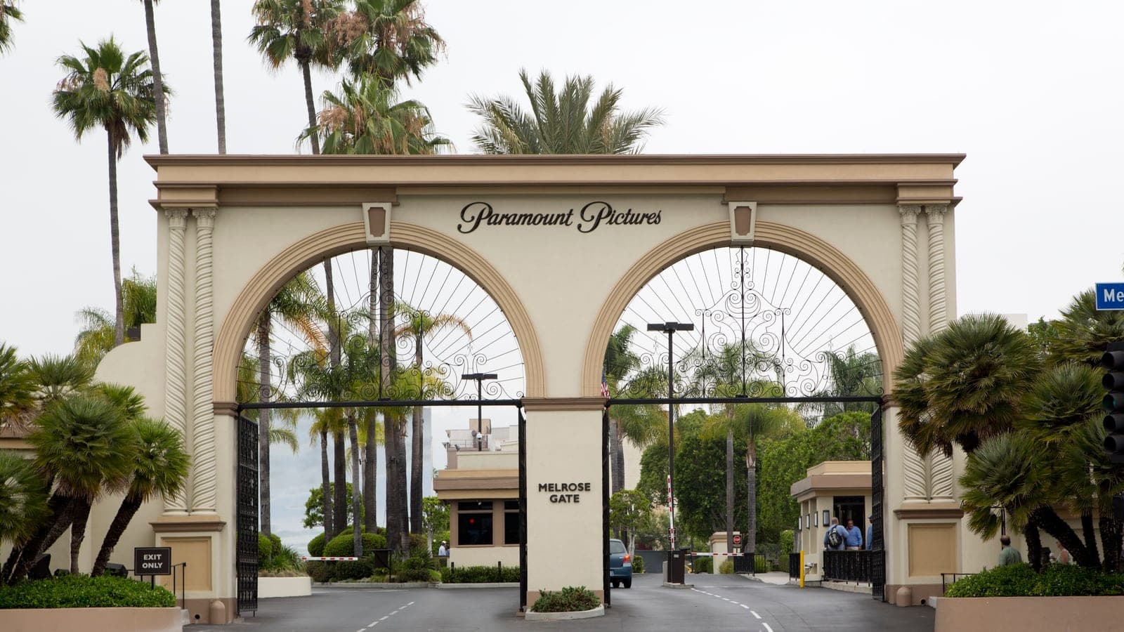 The twin-arched Melrose Gate at the entrance to the Paramount Pictures lot in Hollywood, with palm trees rising behind it and a guard booth beside the empty driveway.