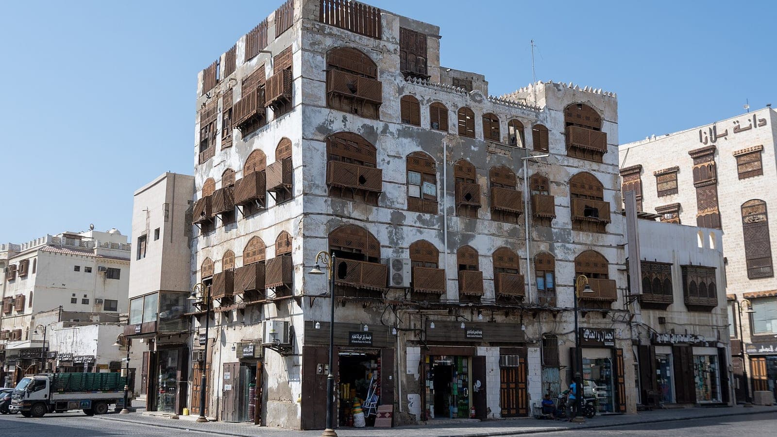 A coral-stone merchant house with carved wooden roshan balconies and shops at street level, on a corner in Al-Balad, the historic district of Jeddah where the Red Sea International Film Festival is staged.