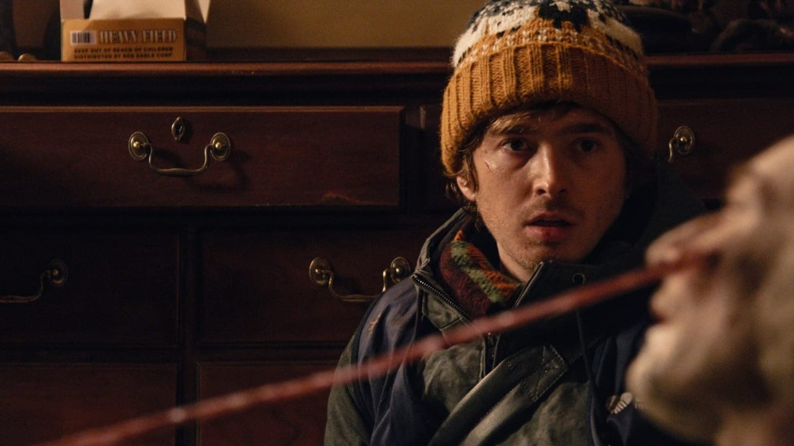 Austin Abrams in a knitted bobble hat and winter coat stares at a figure in the foreground, in a still from Zach Cregger's Resident Evil