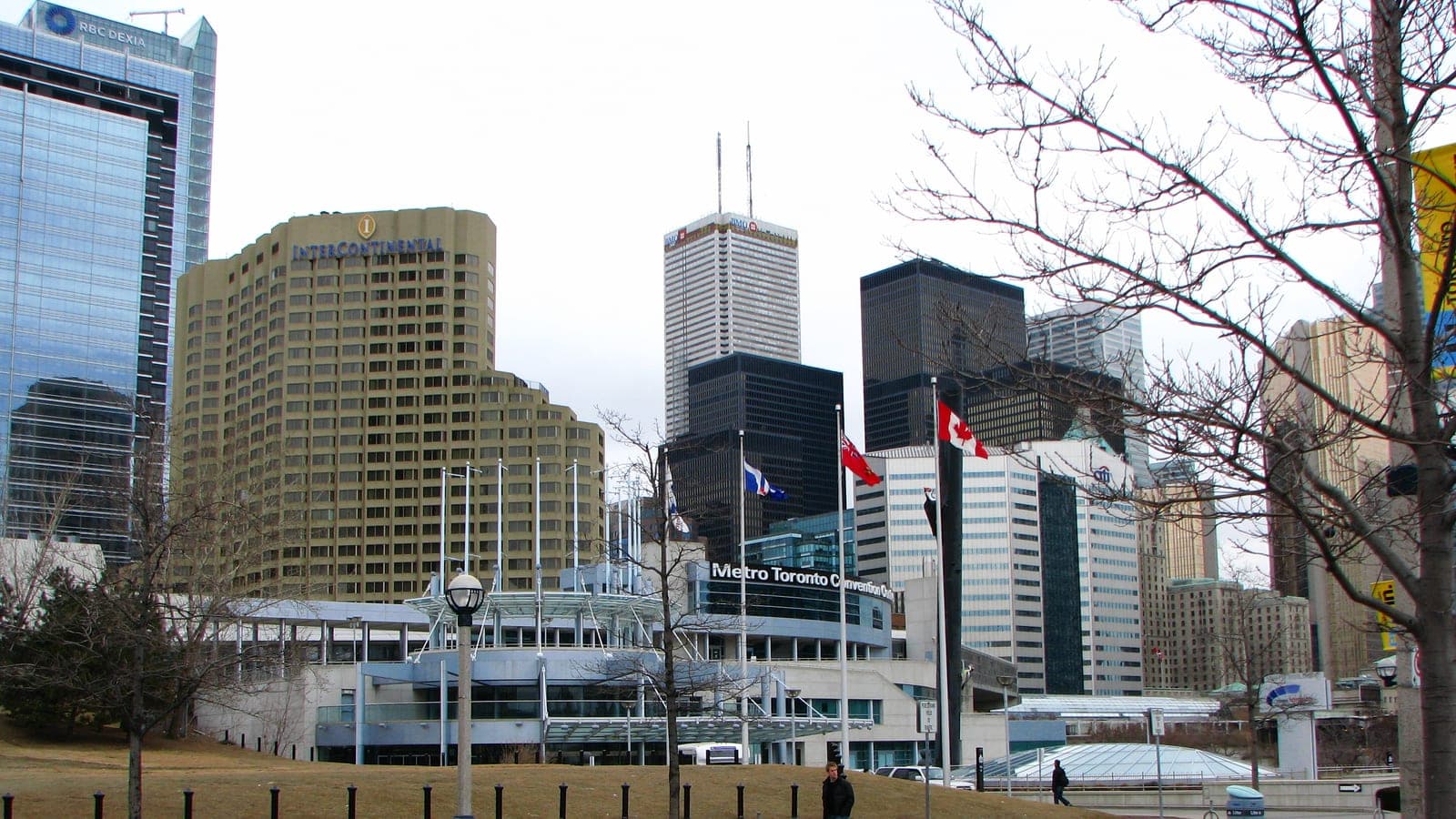 The Metro Toronto Convention Centre's south building, its name lettered above the entrance, with flagpoles in front and the towers of Toronto's financial district behind.